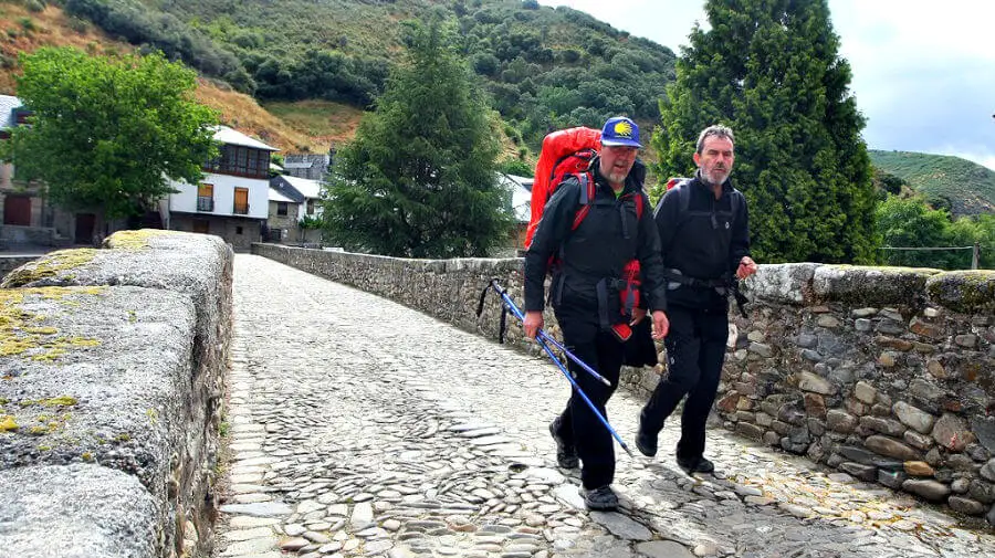 Dos peregrinos cruzando el puente medieval en Molinaseca, León - Camino Francés :: Guía del Camino de Santiago