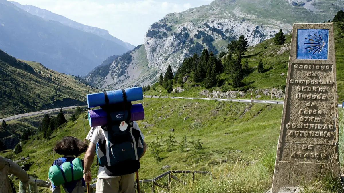 Dos peregrinos junto al mojón del Alto de Somport, inicio del Camino Aragonés, con las montañas del Pirineo al fondo