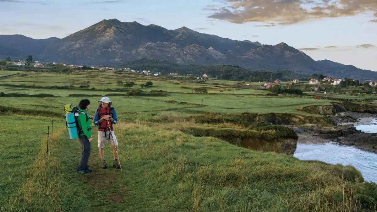 Peregrinos caminando por una etapa del Camino del Norte entre montañas y costa asturiana